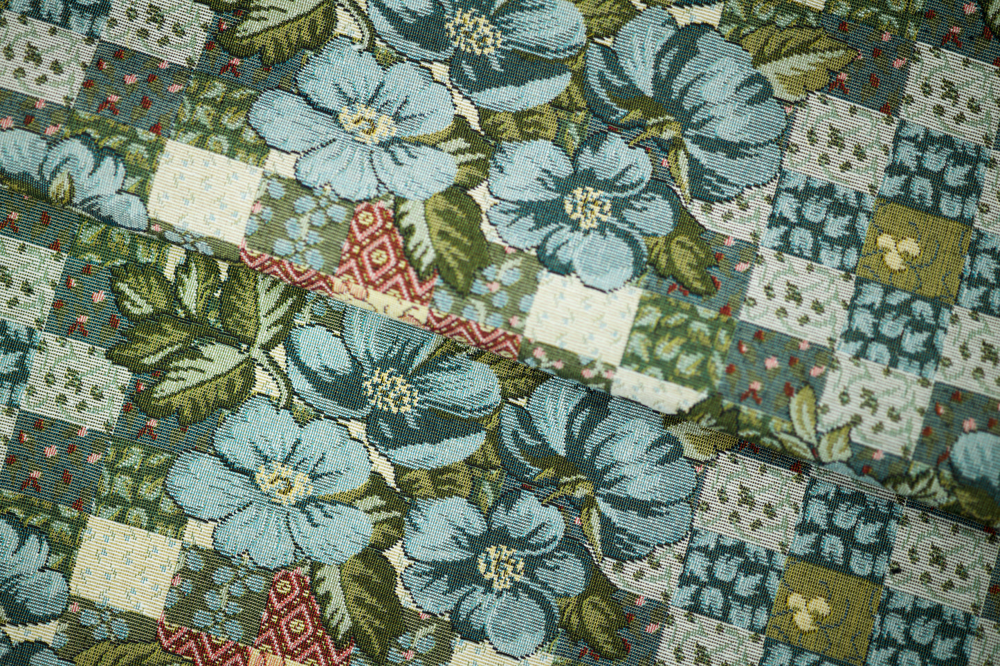 Bunter Möbelstoff mit Patchwork-Optik und blauen Blumen auf hellem Grund – perfekt für kreative Polsterprojekte