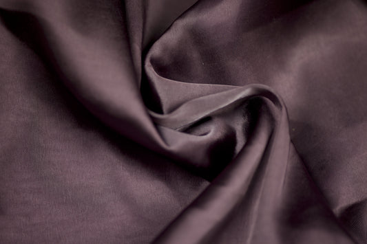 Nahaufnahme eines luxuriösen Satinstoffs in pflaumenfarbener Optik mit seidigem Glanz und weichem Faltenwurf – ideal für elegante Kleidung und kreative Projekte.